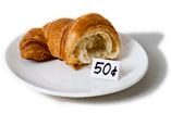 Half a croissant, on a plate, with a sign in front of it saying '50c'